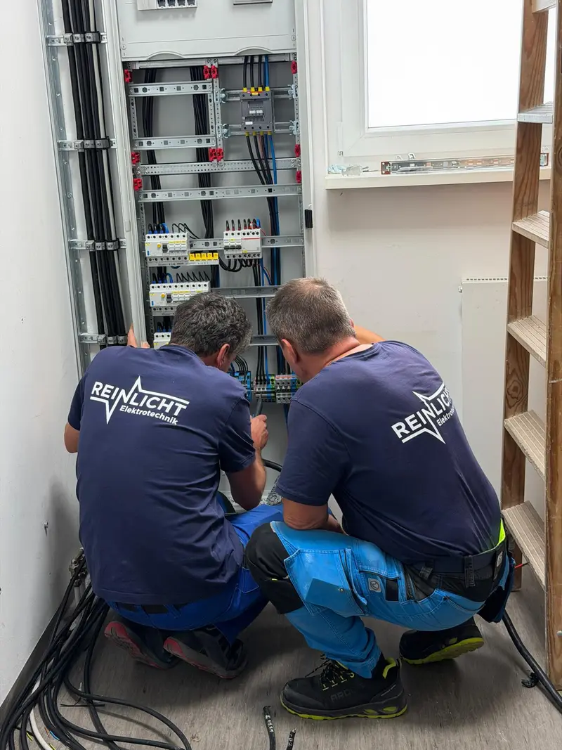 Zwei Monteure von Reinlicht Elektrotechnik verdrahten kniend einen großen Verteilerschrank