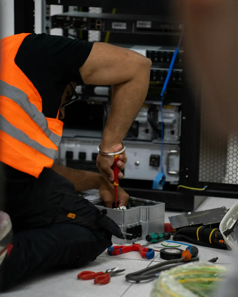 Techniker in Warnweste arbeitet mit Werkzeug an einem Netzwerkschrank